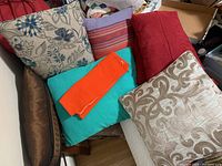Overview of the six pillows arranged together showing variety of colors and patterns including bright orange and green pillow cases and multiple patterned throw pillows.