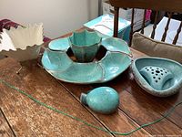 Wide view of all four pottery items on wooden table: leaf tray, flower pots, vase