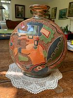 View of the round red clay pottery vessel showing colorful, detailed Mayan god carving on one side.