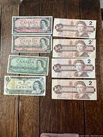 Lot of six $2 Canadian bills and two $1 Canadian bills laid out on wooden surface, showing front sides.