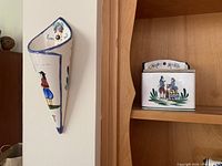 Wall mounted cornet-shaped ceramic wall pocket handpainted with Breton figure and floral motifs in bright colors.