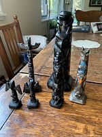 Five totem pole figurines including tall black carved pieces and a colorful wooden totem pole on a wood table