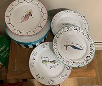 Four round dessert plates decorated with colorful vintage shoes and French phrases displayed with striped round storage box