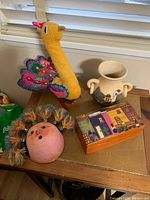 Overview of South American items including textile bird, ceramic vase, coconut mask, and hand-painted box on wooden surface near window