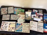 Wide view of multiple binder pages and loose stamps arranged on table, showing partial collection including binders with mounted stamps and sheets.