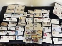 Wide view of approximately 40+ first day covers and envelopes laid out on a surface plus several binders shown