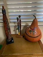 Three tribal art pieces including one tall Maasai tribe gourd with beadwork on metal stand and leather, carved wooden statue of two figures with paint accents, and a large gourd decorated with beads, textile, and burnt designs signed by artist.