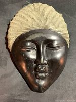 Close-up front view showing polished black opal stone face with expression and rough textured headdress