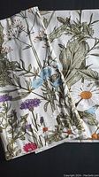 Photo showing a close-up of the fabric with multi-colored floral prints including blue, purple, white, and orange flowers on green stems and leaves.