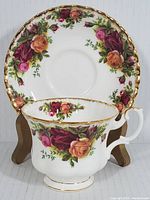 Tea cup and saucer displayed on wooden stands showing floral rose pattern and gold trim under natural light.