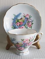 Front angled view of tea cup in front of decorated saucer showing floral and house design