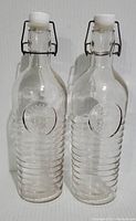 Two clear Bormioli Rocco Officina glass water bottles with white sealing caps and metal clamp mechanisms visible, standing upright side by side.