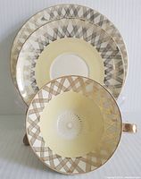 Cup displayed face-up alongside saucer showing gold geometric pattern and gilt handle