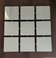 Top-down photo of the assembled large square panel mirror placed on wooden floor. Reflective and solid white panels visible.