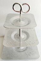 Front view of three-tier serving tray showing etched rose patterns on all tiers and loop handle at top.