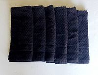 Top view of six folded black hand towels showing textured checkerboard weave pattern.