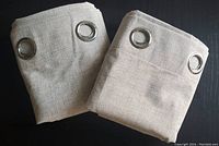 Two folded light beige blackout curtain panels with silver metal grommets.
