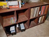 Two wooden shelves each with 4 compartments, some containing records and CDs. Shelves show surface wear like scuffs and scratches.