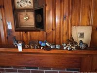 Wide shot of ceramic and stone animal, bird, and horse figurines displayed on a wooden mantel beneath a clock, including a book on sculpture.