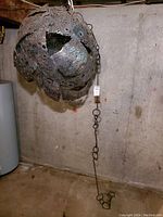 Photo of large spherical forged steel metal sculpture with intricate plasma cut decorative latticework hanging in basement; heavy steel chain attached for hanging.