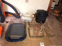 View of all bakeware items including glass baking dishes, casserole dishes, measuring cup, and double boiler pot on carpeted floor