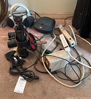 Photo shows two CD players, two pairs of binoculars, microscope lenses, pencil sharpener, and various power cords and surge protectors on carpet.