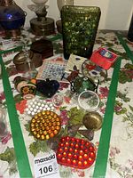 Collection of glass trinkets laid out on floral cloth, showing marbles, dishes, brass door knob, and small glass pieces