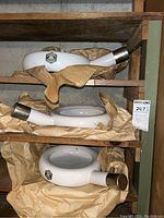 Three white enamelware bed pans stacked on wooden shelves, each with a cylindrical metal-rimmed spout, wrapped in protective paper, showing Ker brand logo.
