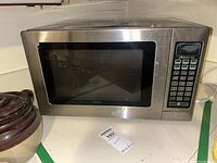 Haier microwave oven closed showing stainless steel exterior and keypad control panel on right side.