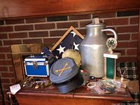 Overview of the lot showing military framed/unframed flags, uniform hat, canteen, blue metal case, trophies, pins, medals, and jug.