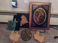 Photo showing entire lot with large framed religious plaque, multiple small sculpted religious figures including busts and praying hands, and one oval decorative relief plaque.