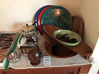 Overview of wooden bowls, elongated platters, colorful serving trays, glass and metal fondue set, spherical wooden item, and small bowls and cups.