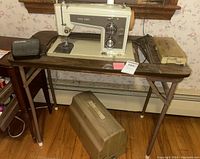 Full view of vintage Sears Kenmore sewing machine mounted on wooden table with carrying case beside it on the floor.