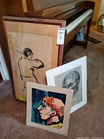 Three artworks including framed ink drawing of musician, acrylic painting, and pencil portrait; piano in background