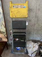 Yellow folding step ladder with black steps shown against a concrete wall.