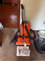 Orange Kenmore HEPA vacuum cleaner and accessories including hose, wand, nozzle, and instruction manuals on carpeted floor.
