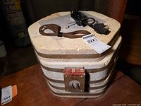 Hexagonal vintage ceramic kiln with insulating firebrick walls and metal clamps, showing front control panel with dual knobs. Kiln top has two cords placed on it, one brown and one black.