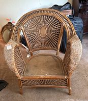 Front view of wicker chair showing rounded detailed back and armrests, seat area with wear evident.