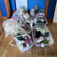 Overall view of multiple bins holding yarn skeins in different colors and types, including plastic bags and a partially completed knitted item