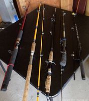Five fishing poles shown standing upright on a black table, displaying various styles of grips and rod colors.
