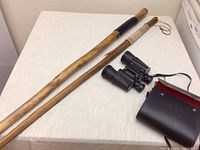 Two wooden walking sticks and Mercury brand binoculars with black carrying case on a white surface.