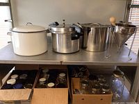 Photo shows all items on metal shelving including the jars in boxes below and all pots and funnel on top shelf