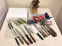 Full view of knives laid out alongside two cutting boards and two knife sharpeners. Wooden Chicago Cutlery block holds several knives.