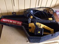 McCulloch electric chainsaw in its branded black protective carrying case with power cord visible, placed on a shelf.