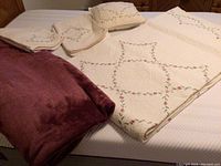Full view of the quilted white bedspread with floral embroidery, matching pillow sham and valances, and soft dark mauve fleece blanket on bed surface.