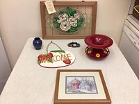 Overall lot view with all items including framed glass art, welcome sign, blue vase, hummingbird feeder, small floral decor and framed print.