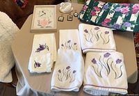 Overview of floral embroidered towels, seat cushions, ceramic swan figurine, wall clock and plaques.