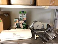 Rival meat slicer and FoodSaver vacuum sealer together on a countertop with packaging for seal rolls visible behind