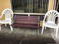 Photo showing two white plastic outdoor chairs placed on either side of a wooden and metal garden bench with dark brown slats.
