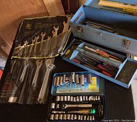 Overview of wrench set in fabric roll, adjustable wrenches, socket set case, and open metal toolbox with screwdrivers inside.